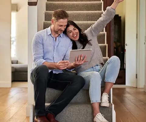 Happy couple sitting on stairs looking at tablet together